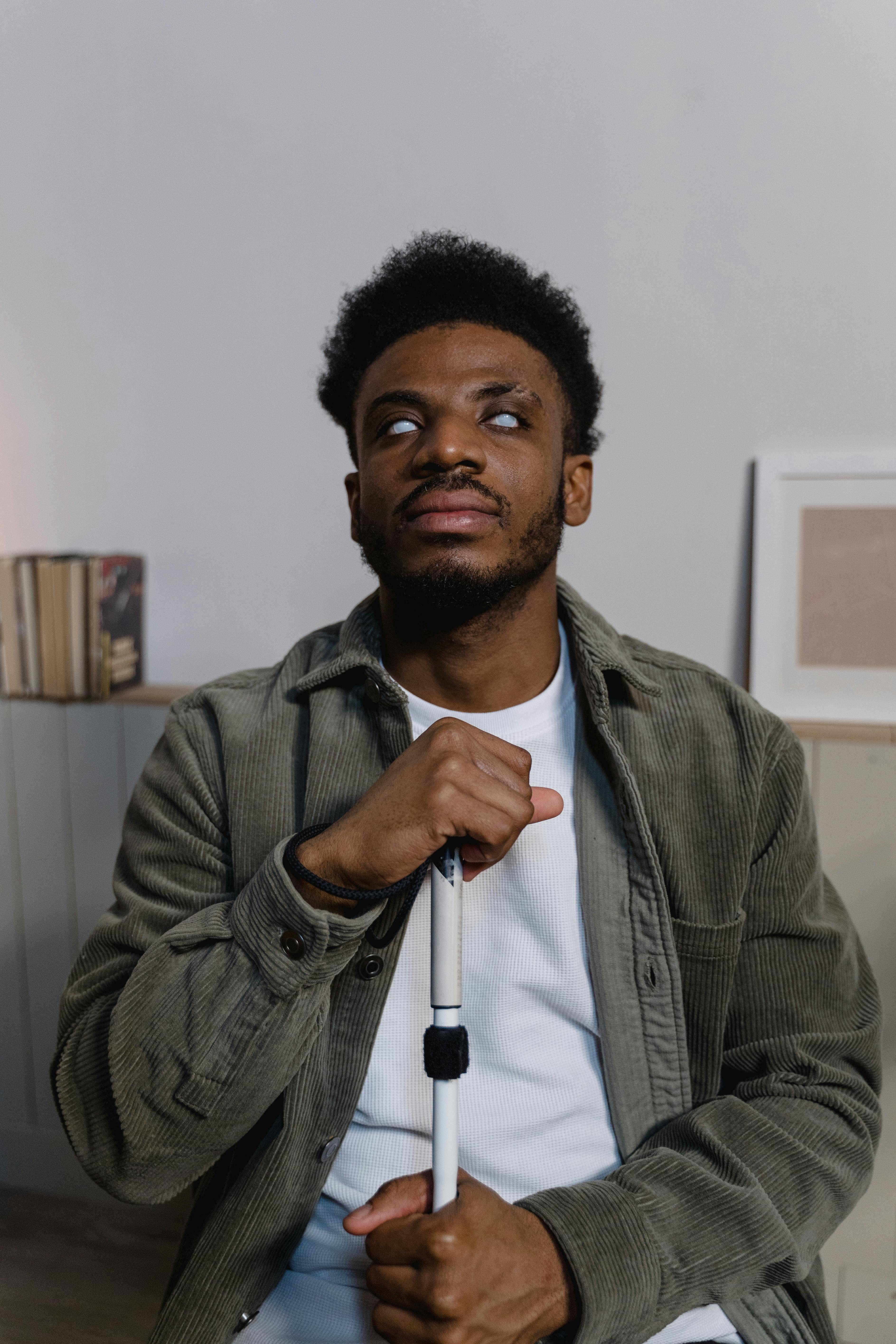image of a blind  person seated holding a white cane towards his chest 